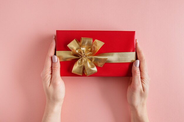 Frau, die Geschenkbox mit goldenem Band in den Händen auf rosa Hintergrund hält