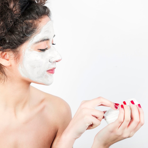 Frau, die Gesichtsmaske auf ihrem Gesicht gegen weißen Hintergrund anwendet