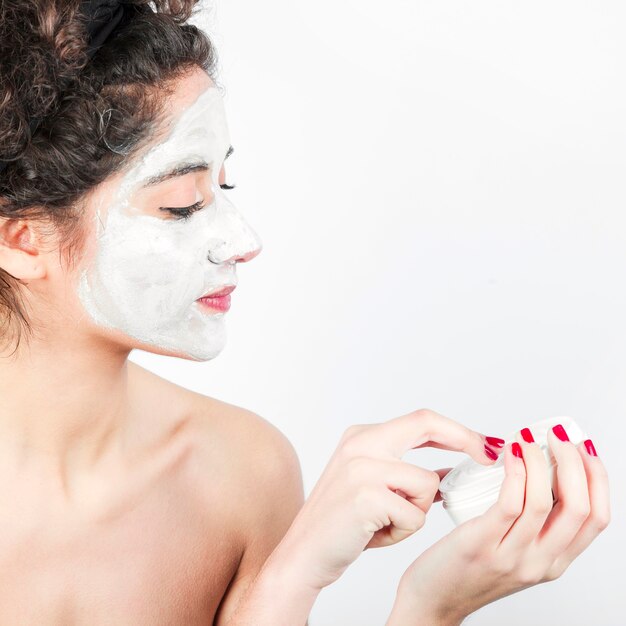 Frau, die Gesichtsmaske auf ihrem Gesicht gegen weißen Hintergrund anwendet