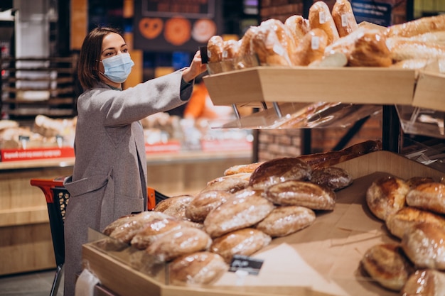 Frau, die Gesichtsmaske trägt und im Lebensmittelgeschäft einkauft