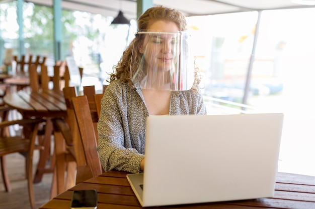Frau, die Gesichtsschutz beim Arbeiten am Laptop trägt