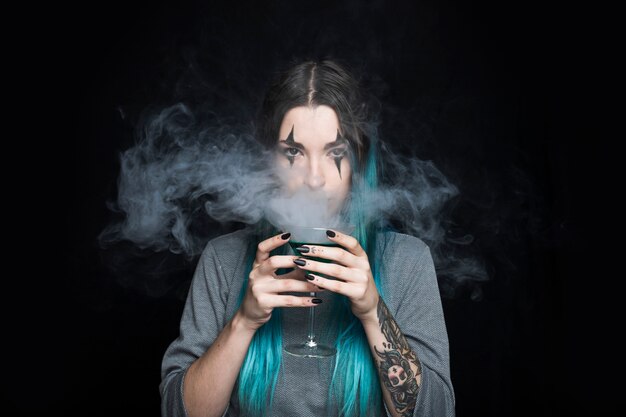 Frau, die Glasbecher mit grüner Flüssigkeit und Rauche hält