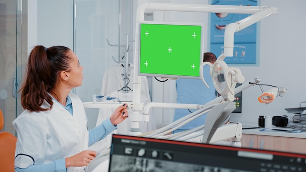 Kostenloses Foto frau, die grünen bildschirm auf monitor und röntgenstrahl der zähne für zahnmedizinische untersuchung analysiert. zahnarzt, der chroma-key und mockup-display zur kontrolle verwendet, während er röntgenaufnahmen für die mundpflege betrachtet