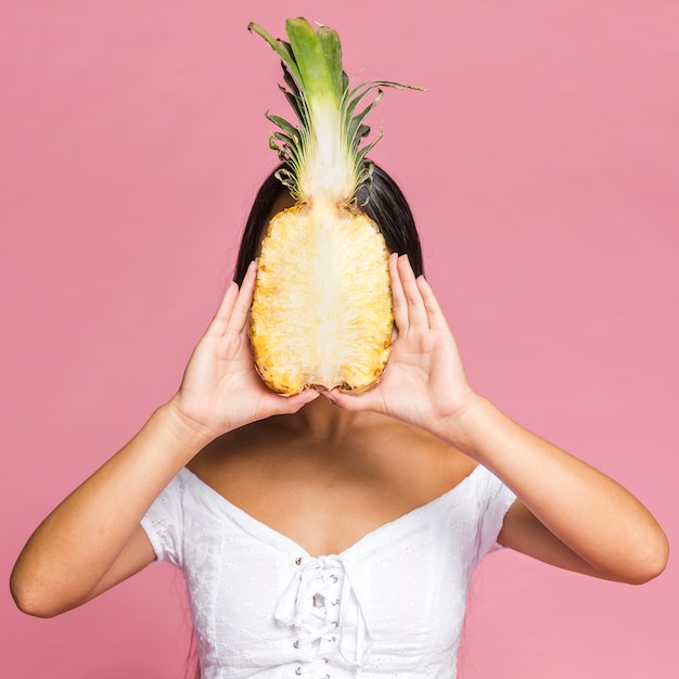 Frau, die hälfte der ananas vor ihrem gesicht hält