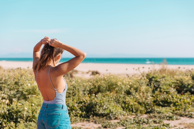 Frau, die Hände hinter Kopf setzt und Meer betrachtet