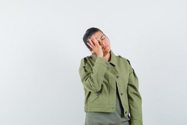 Frau, die Hand auf Gesicht in Jacke, T-Shirt hält und müde aussieht.