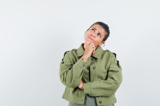 Frau, die Hand auf Kinn in Jacke, T-Shirt hält und zögernd schaut.