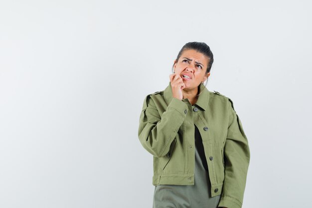 Frau, die Hand auf Kinn in Jacke, T-Shirt hält und zögernd schaut.