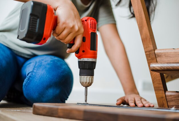 Frau, die Handbohrmaschine verwendet, um einen Holztisch zusammenzubauen