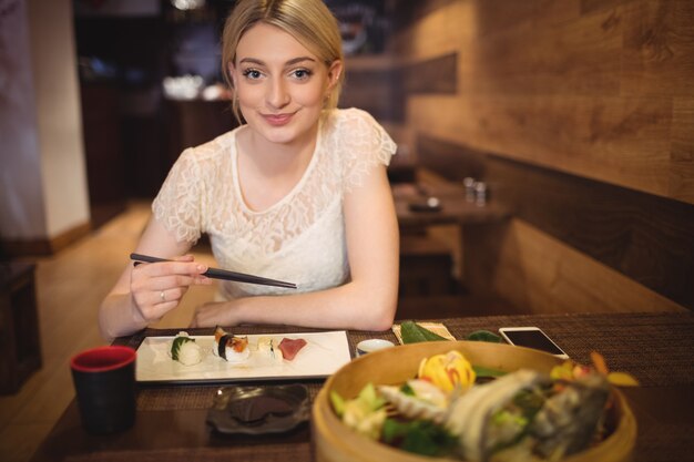 Frau, die Handy beim Essen von Sushi verwendet