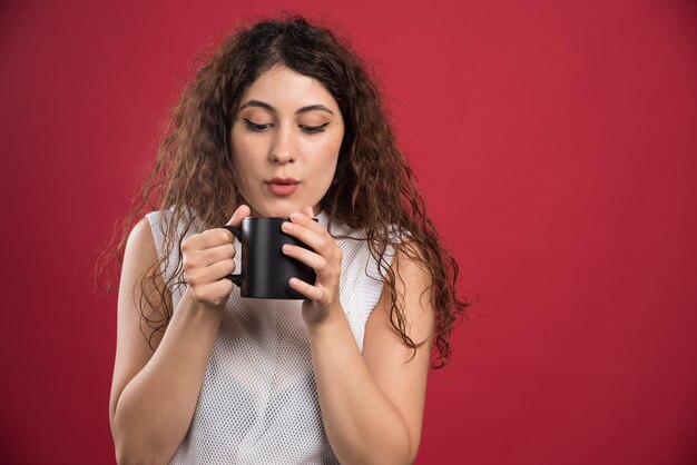 Frau, die heiße dunkle Tasse auf Rot hält