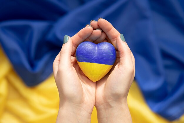 Frau, die Herz mit ukrainischer Flagge über einer anderen Flagge hält