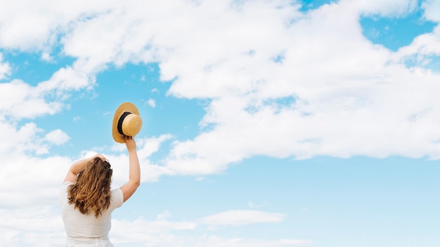 Frau, die Hut hält, der Wolken im Himmel bewundert