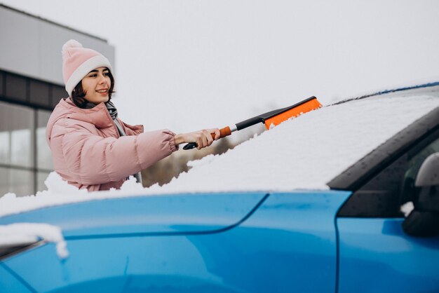 Frau, die ihr Fensterauto vom Schnee säubert