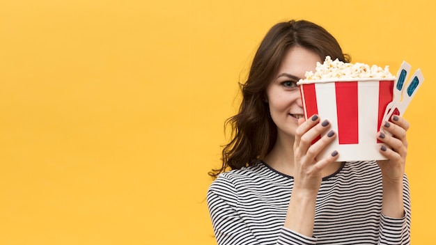 Frau, die ihr Gesicht mit 3D-Brille und Eimer mit Popcorn bedeckt