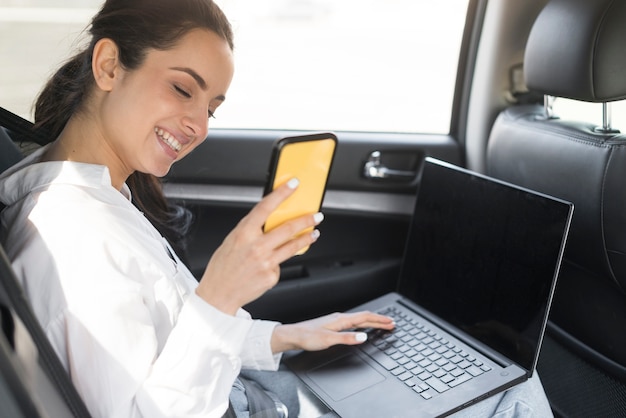 Frau, die ihr Handy und Laptop im Auto benutzt