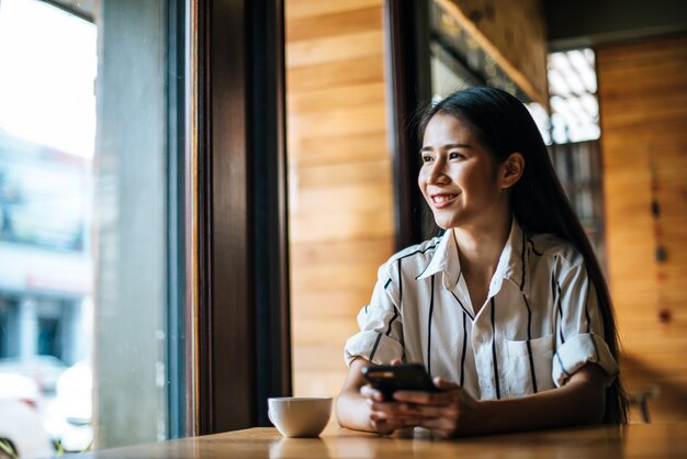 Frau, die ihr intelligentes Telefon am Café sitzt und spielt