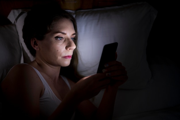 Frau, die ihr Telefon hält, während sie im Bett bleibt