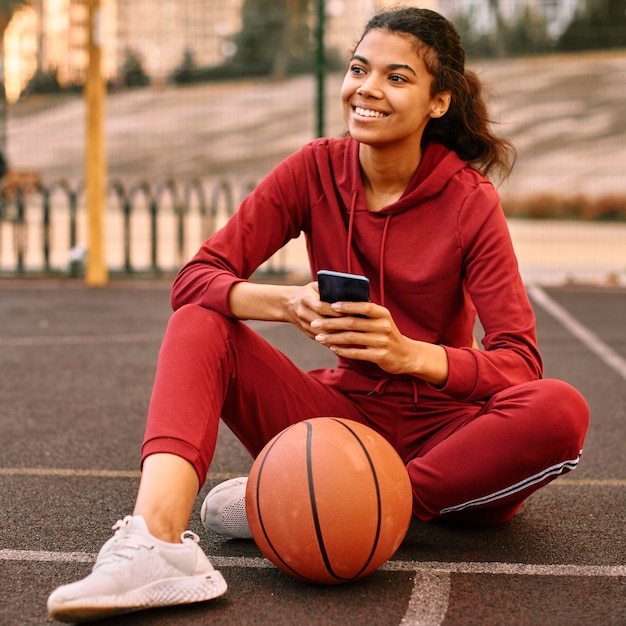 Frau, die ihr Telefon neben einem Basketball überprüft