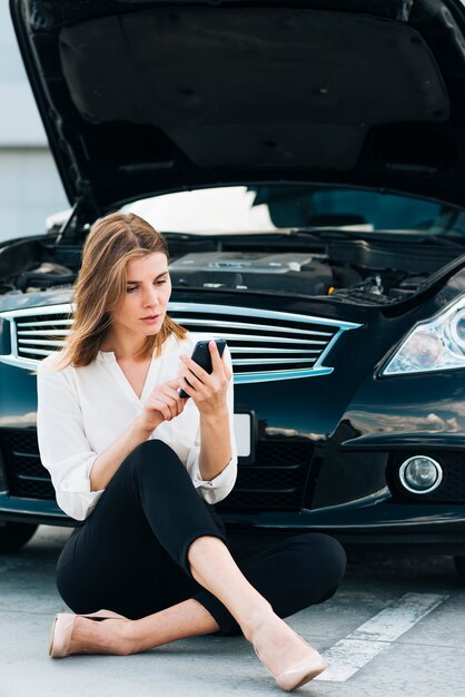 Frau, die ihr Telefon und schwarzes Auto überprüft