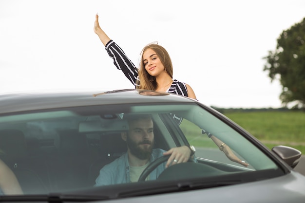 Frau, die ihre Hand von außerhalb des Autofensters wellenartig bewegt