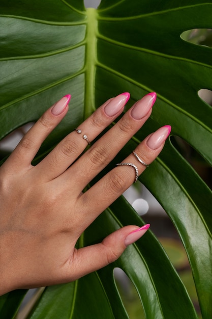 Kostenloses Foto frau, die ihre nagelkunst auf fingernägeln gegen monsterblatt zeigt