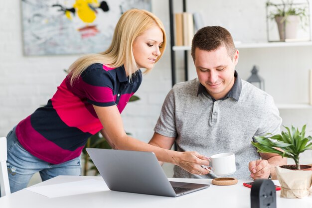 Frau, die ihrem Ehemann Kaffee gibt, der an Laptop arbeitet