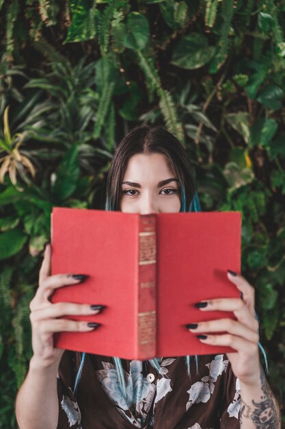 Frau, die ihren Mund mit dem Buch steht gegen wachsende Anlage bedeckt