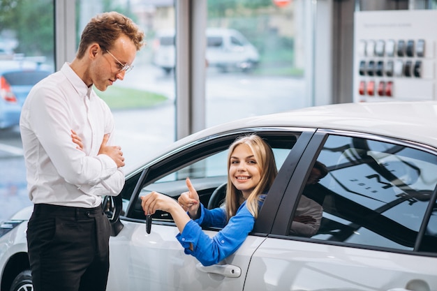 Frau, die im Auto sitzt und Schlüssel in einem Autosalon empfängt