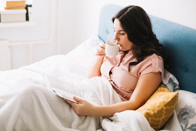 Frau, die im Bett liest und trinkt