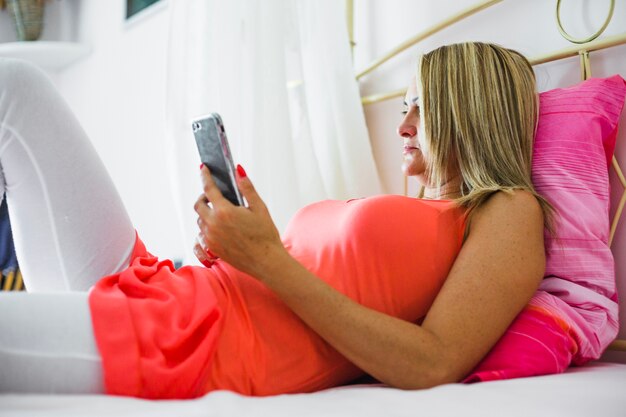 Frau, die im Bett mit Telefon kühlt