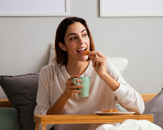 Frau, die im Bett zu Hause frühstückt