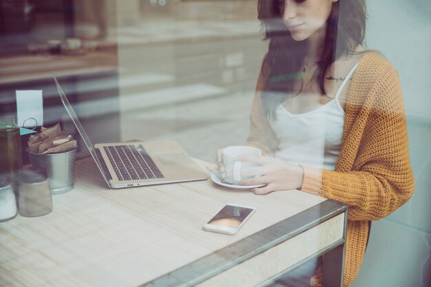 Frau, die im Café mit Kaffee und Laptop stillsteht