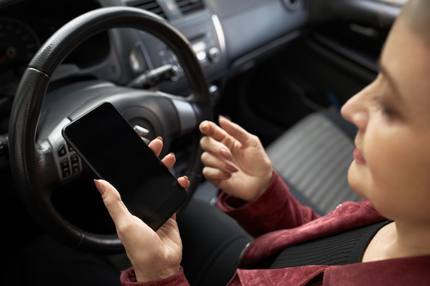 Frau, die im Fahrersitz mit Handy sitzt