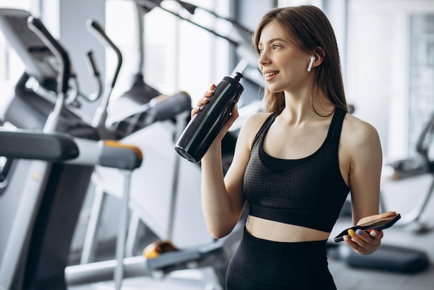 Frau, die im Fitnessstudio Musik hört und Wasser trinkt