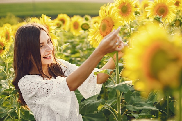 Frau, die im Sonnenblumenfeld steht. Brünette Frau trägt weiße Kleidung im Sommerfeld