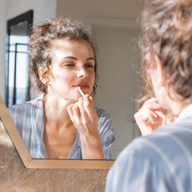 Frau, die im Spiegel schaut und Lippenstift anwendet