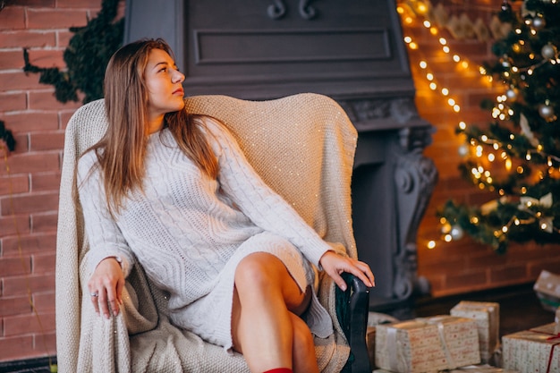 Frau, die im Stuhl durch Weihnachtsbaum sitzt