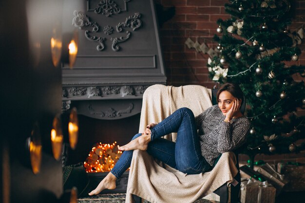 Frau, die im Stuhl durch Weihnachtsbaum sitzt