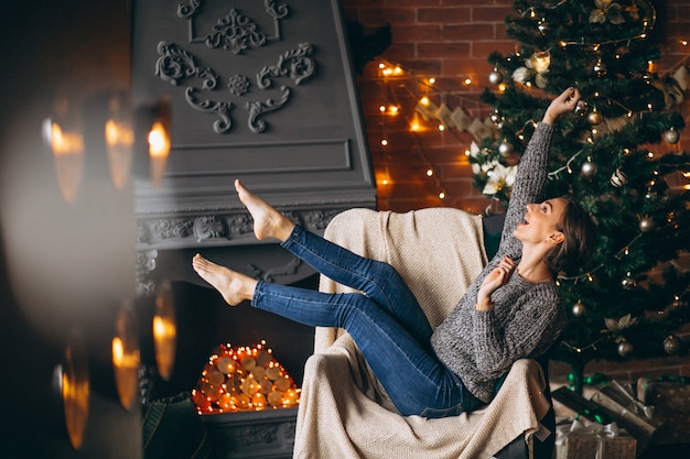 Frau, die im Stuhl durch Weihnachtsbaum sitzt