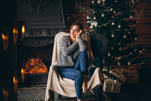 Frau, die im Stuhl durch Weihnachtsbaum sitzt