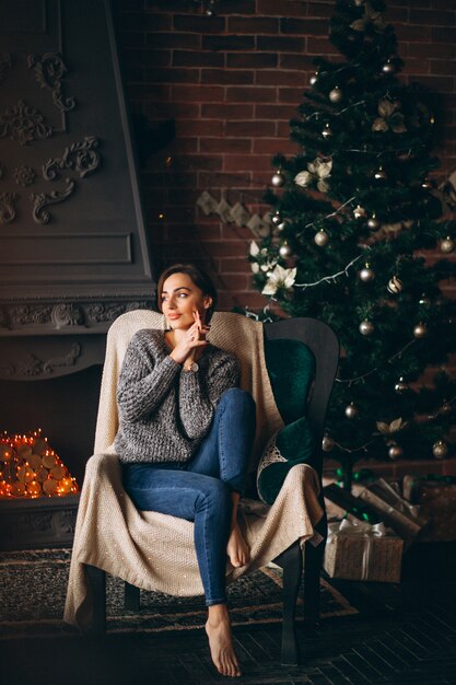 Frau, die im Stuhl durch Weihnachtsbaum sitzt