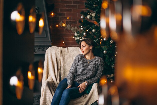 Frau, die im Stuhl durch Weihnachtsbaum sitzt