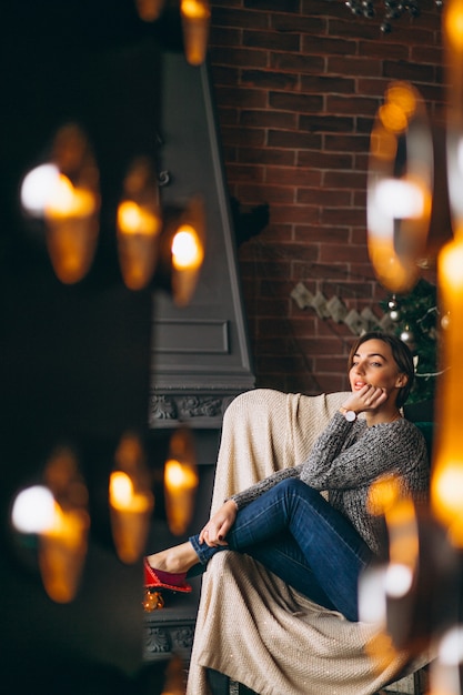 Frau, die im Stuhl durch Weihnachtsbaum sitzt