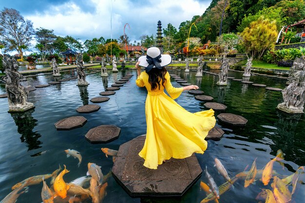 Frau, die im Teich mit buntem Fisch am Tirta Gangga Wasserpalast in Bali, Indonesien steht