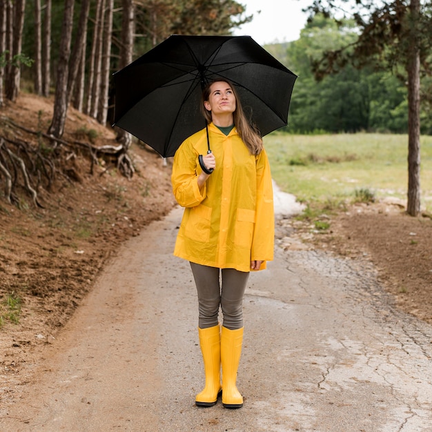 Kostenloses Foto frau, die im wald steht, während sie einen regenschirm hält