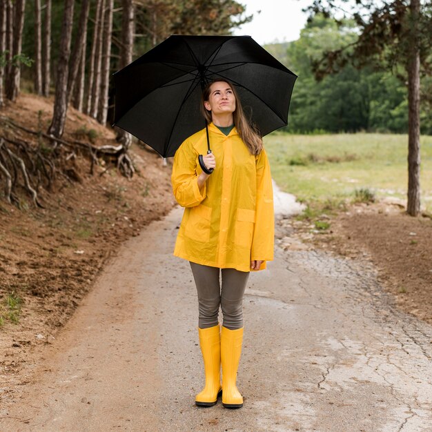 Frau, die im Wald steht, während sie einen Regenschirm hält