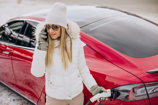 Frau, die im Winter rotes Elektroauto auflädt