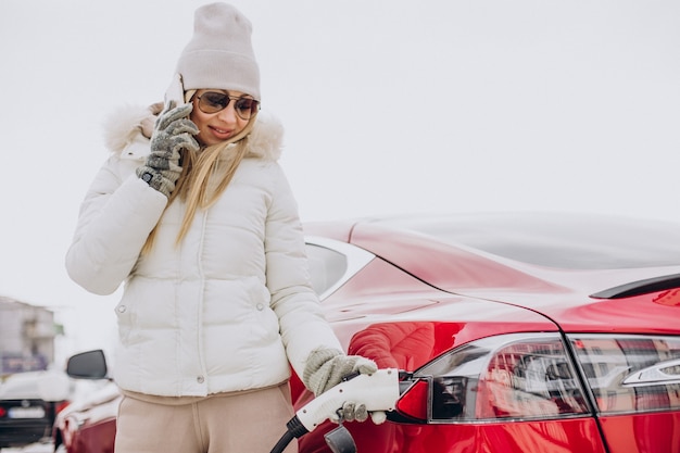 Kostenloses Foto frau, die im winter rotes elektroauto auflädt