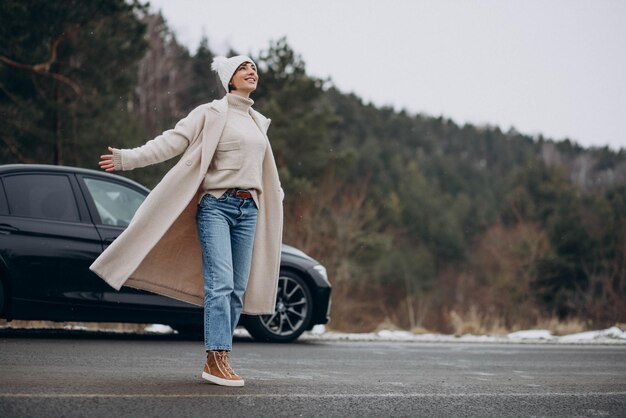 Frau, die im Winterwald mit ihrem Auto die Straße überquert